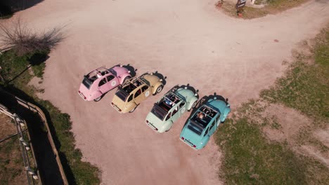 Vista-De-Rotación-Aérea-De-Algunos-Coches-Antiguos-De-Colores-En-Un-Camino-De-Tierra-En-Una-Cola-Utilizada-Como-Atracción-Turística,-Citroën-Cv2