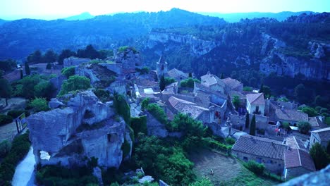 Drohnenaufnahme-über-Einer-Kleinen-Stadt-In-Frankreich-Mit-Häusern-Und-Kirchen-Und-Einer-Wunderschönen-Landschaft-Mit-Felsen-Und-Natur-Im-Hintergrund