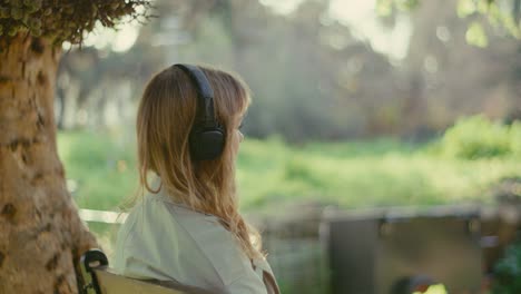 Lonely-lady-on-park-bench-under-tree-with-headphones-listening-to-music
