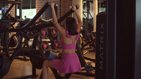 Latina-girl-sits-using-a-weight-lifting-machine-at-the-gym-for-muscles-in-the-back