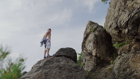 mountain-rock-climber-getting-rid-of-his-shirt,-bouldering-B-roll-shot-in-mountains,-rough-edge-and-ridges-freeclimbing,-sunny-bright-day,-cinematic-scenic-landscape-shot,-handsome-athletic-male