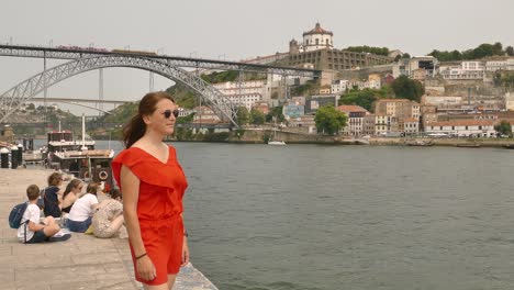 Woman-in-red-dress-standing-by-the-sea-admiring-the-view-from-the-Dom-Luis-bridge-in-Porto,-Portugal