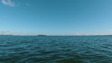 POV-from-small-boat-of-blue-sky-meets-blue-water-with-a-small-island-on-the-horizon