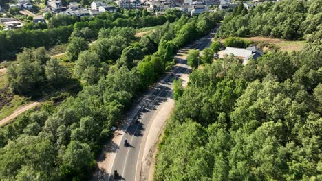 Biker-club-on-the-road-surrounded-by-forest,-aerial-drone-view
