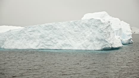Gimbal-shot-around-white-and-blue-iceberg-in-polar-region,-part-of-expedition