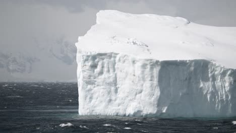 Stormy-day-in-Antarctica,-water-splashing-against-big-ice-berg