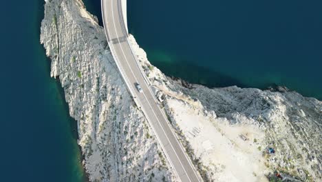 An-aerial-following-road-over-island-Pag-and-bridge-over-beautiful-blue-sea,-summer-in-Croatia