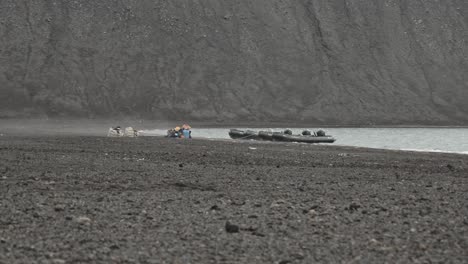 Expedition-zodiac-stranded-on-remote-and-lonely-beach,-with-steam-rising-from-active-volcano