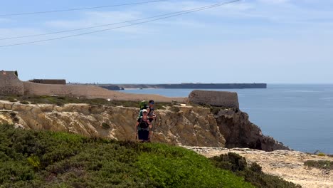 Kamerafahrt,-Die-Ein-Wandererpaar-Mit-Rucksack-Zeigt,-Das-An-Einem-Sonnigen-Tag-Entlang-Der-Gigantischen-Küste-Der-Algarve-Spaziert
