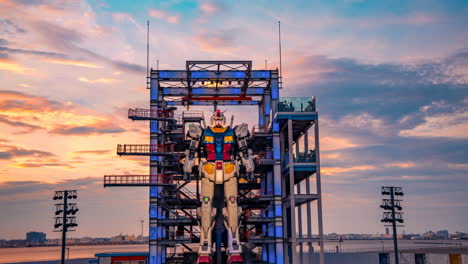 Robot-Mecha-Gundam-Entrando-En-La-Fábrica-Base-En-La-Bahía-De-Yokohama,-Tokio,-Modo-De-Espera,-Lapso-De-Tiempo-En-Movimiento-Al-Atardecer