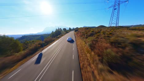 FPV-aerial-following-a-white-Porsche-through-a-scenic-mountain-landscape