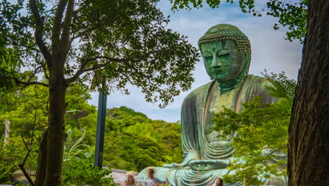 Moving-zoom-in-Timelapse-Great-green-buddha-of-Kamakura-bronze-Daibutsu-Japan-between-trees-and-Green-leaves-cloudy-summer-day