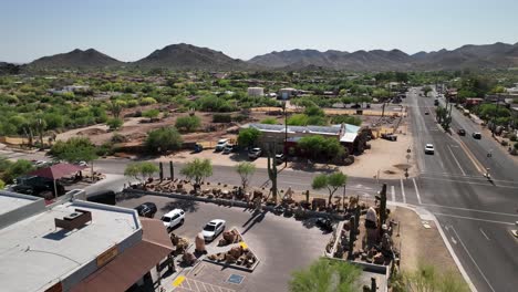 Tiro-De-Drones-Bajando-De-Un-Estacionamiento-En-Arizona-Decorado-Con-Cactus-Y-Esculturas-De-Arcilla