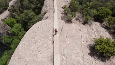 zenithal-aerial-drone-shot-of-a-young-woman-descending-the-stairs-of-the-natural-park-of-the-mountains-of-montserrat,-concept-of-health-and-sport-outdoors