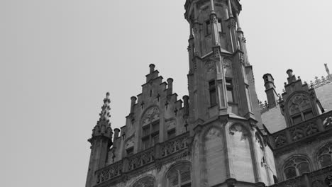 Grayscale-Shot-Of-Gothic-Tower-Of-The-Historium-Building-During-Daytime-In-Bruges,-Belgium