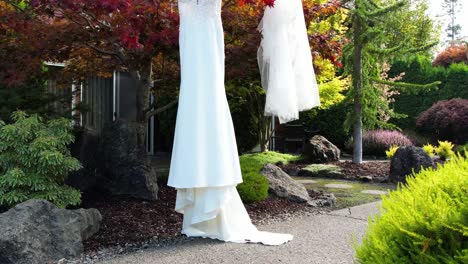 Romantic-drone-flight-captures-a-white-wedding-dress-hanging-from-a-tree,-set-amidst-a-picturesque-outdoor-setting