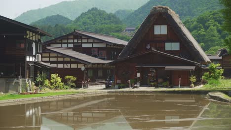 Teilweise-überflutetes-Feld-Mit-Blick-Auf-Traditionelle-Dorfhäuser-Und-Gebäude-Mit-Strohdächern-In-Shirakawago-Im-Hintergrund