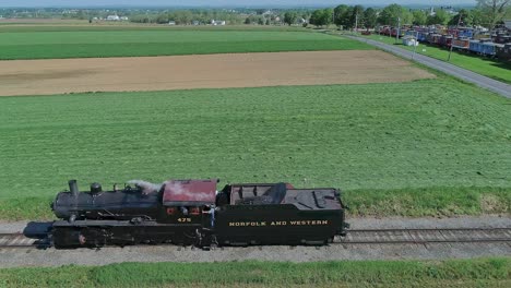 Una-Vista-Lateral-De-Una-Locomotora-De-Vapor-Que-Viaja-Sola-En-Una-Prueba-A-Través-Del-Campo-Rural-En-Una-Sola-Vía,-Con-Un-Ingeniero-Y-Un-Bombero-Observando,-En-Cámara-Lenta-En-Un-Día-De-Primavera