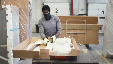 An-Ashley-Furniture-HomeStore-warehouse-merchandise-worker-unpacks-a-Box-containing-cardboard-and-Styrofoam-on-a-workbench-inside-a-shipping-distribution-center
