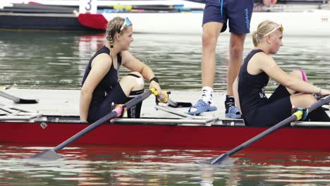 Dos-Mujeres-Con-Jerseys-Bajando-Del-Muelle-Hacia-Un-Doble-Scull-De-Carreras