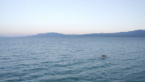 Aerial-orbits-small-fishing-boat-on-Aegean-Sea-waves,-blue-sky-horizon