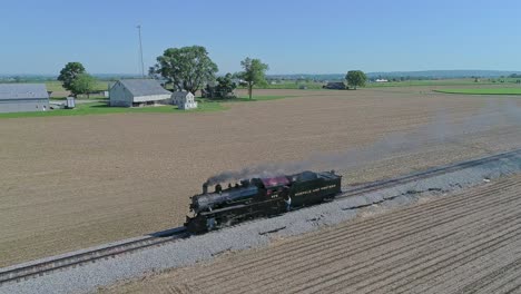 A-Drone-View-of-a-Steam-Locomotive-Traveling-by-Itself-on-a-Test-Run-Thru-Rural-Countryside-on-a-Single-Track,-With-Engineer-Hanging-on-the-Side,-in-Slow-Motion-on-a-Spring-Day