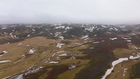 Aerial-panoramic-view-of-mountains-with-melting-snow,-on-a-cloudy-and-foggy-day,-Iceland