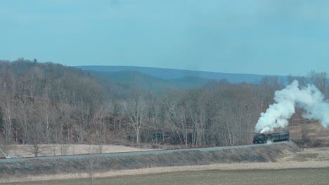 A-View-of-a-Restored-Narrow-Gauge-Steam-Passenger-Train-Approaching-Around-a-Curve,-Blowing-Smoke-and-Steam-on-a-Winter-Day