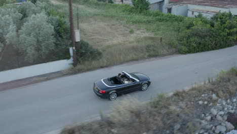 Aerial-tracks-shiny-black-convertible-with-two-young-men-on-coast-road