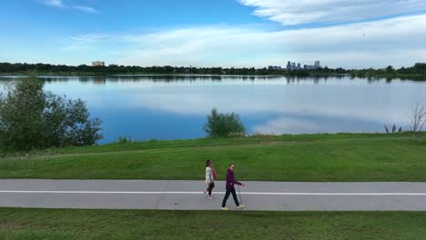 Young-couple-walking-on-path-beside-lake-outside-of-large-American-city
