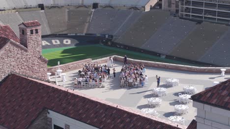 Outdoor-Wedding-Ceremony-on-Sunny-Day,-Static-Drone-Shot-of-Wedding-Couple-and-Guest-on-Terrace-of-Folsom-Field-Stadium,-CU-Boulder-Campus