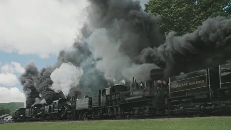 A-Low-View-of-a-Five-Connected-Shay-Steam-Engine,-Approaching,-Blowing-Lots-of-Smoke-and-Steam,-Passing-Freight-Cars-on-a-Sunny-Summer-Day