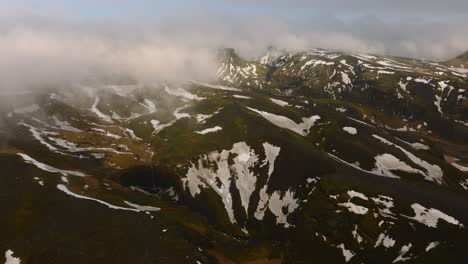 Vista-Aérea-Del-Paisaje-De-Una-Cascada-En-Las-Montañas-Islandesas-Con-Nieve-Derretida,-En-Un-Día-Nublado-Y-Brumoso