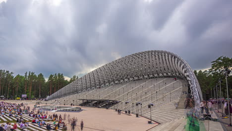 Timelapse-shot-of-huge-crowd-gathering-to-watch-Latvian-Song-and-Dance-Festival-in-an-outdoor-stadium-with-cloud-movement-in-the-background