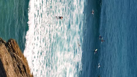 Vertical-handheld-Wide-Shot-of-Surfers-Riding-High-Waves-at-Suluban-Beach,-Bali-in-Slow-Motion