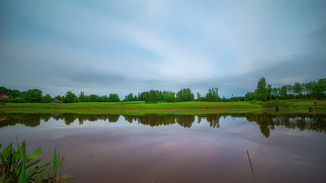 Timelapse-shot-of-dark-cloud-movement-over-a-large-lake-along-rural-landscape-with-green-vegetation-on-a-cloudy-day