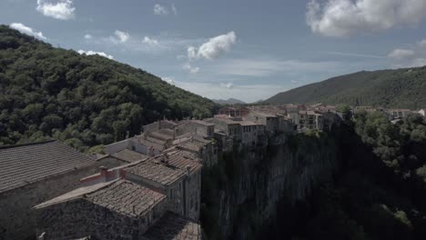 Drone's-panoramic-video-showcases-the-breathtaking-beauty-of-Castellfollit-de-la-Roca,-Spain:-medieval-village-perched-atop-a-striking-volcanic-cliff