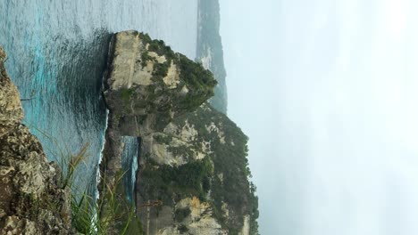 Vertical-dolly-forward-reveal-shot-of-Diamond-Beach-on-Nusa-Penida,-Bali,-from-the-cliffs-above-revealing-a-white-sand-beach-and-slow-rolling-swells