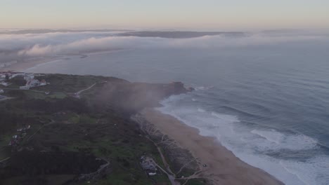 Drone-view-of-Praia-do-Norte-at-Nazaré-with-low-clouds-during-sunrise,-aerial
