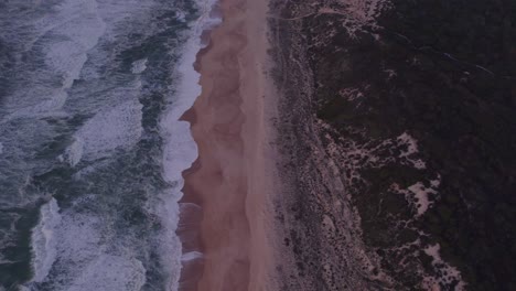 Flying-forward-over-empty-Praia-do-Norte-Nazaré-Portugal-during-sunset,-aerial