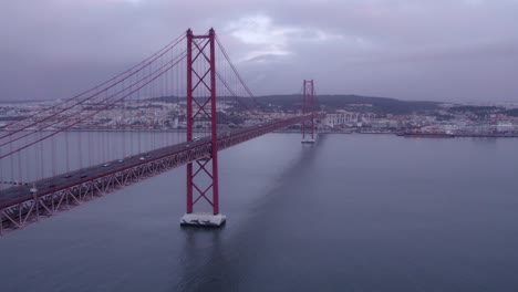 Flying-next-to-the-Ponte-25-de-Abril-famous-bridge-during-a-cloudy-morning,-aerial