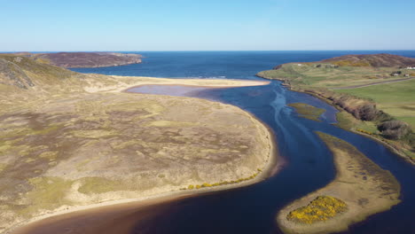 Drone-travelling-over-a-beautiful-river-estuary-leading-out-to-sea,-on-the-north-coast-of-Scotland