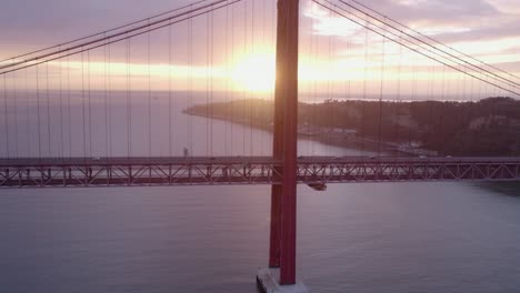 Sun-reveals-behind-Ponte-25-de-Abril-bridge-pilar-at-sunrise,-aerial