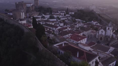 Historic-walled-town-of-Obidos-Portugal-during-colourful-sunrise,-aerial