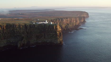 Aerial-shot-of-a-stunning-lighthouse-perched-high-above-calm-seas-at-sunrise-in-Scotland