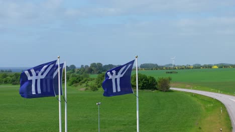 Flags-of-Ystad,-Sweden-city,-waving-in-stormy-wind,-beautiful-green-landscape