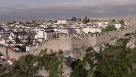 Flying-backwards-old-city-wall-of-Obidos-Portugal-in-morning-light,-aerial