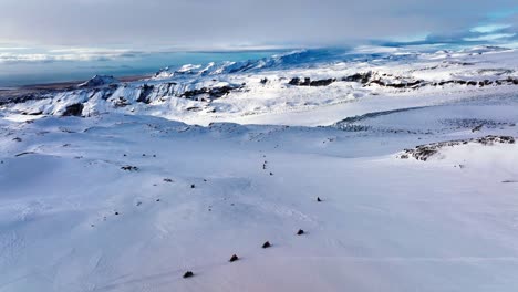 Aerial-panoramic-landscape-view-of-people-riding-snowmobiles-on-the-frozen-ground-of-Myrdalsjokull-glacier-in-Iceland,-at-dusk
