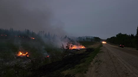 Anhaltender-Waldbrand-Auf-Freiem-Feld,-Während-Feuerwehrautos-Auf-Einer-Unbefestigten-Straße-Vorbeifahren