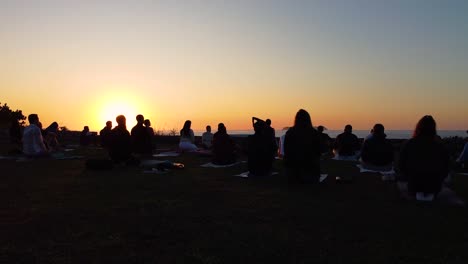 Group-of-people-doing-yoga-during-sunset,-view-from-behind